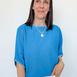 Woman wearing a blue top and white pants against a plain background