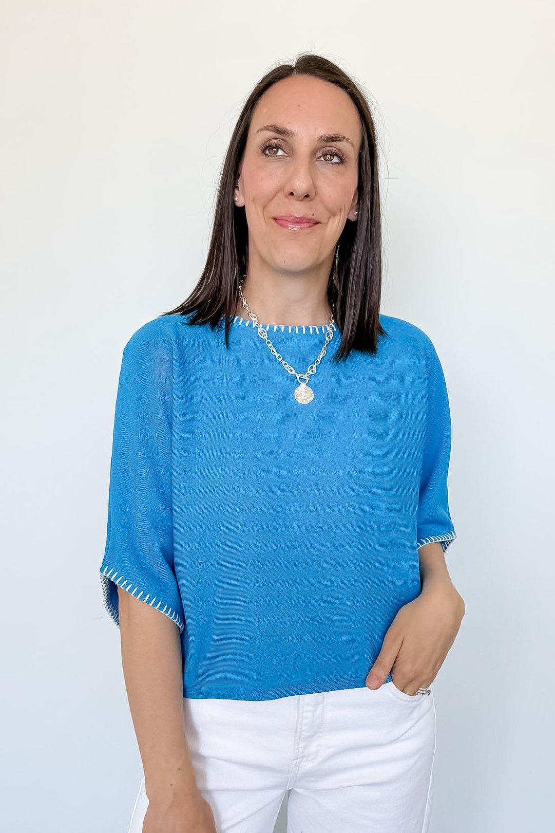 Woman wearing a blue top and white pants against a plain background
