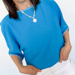 Woman wearing a blue top with white trim and white pants against a white background