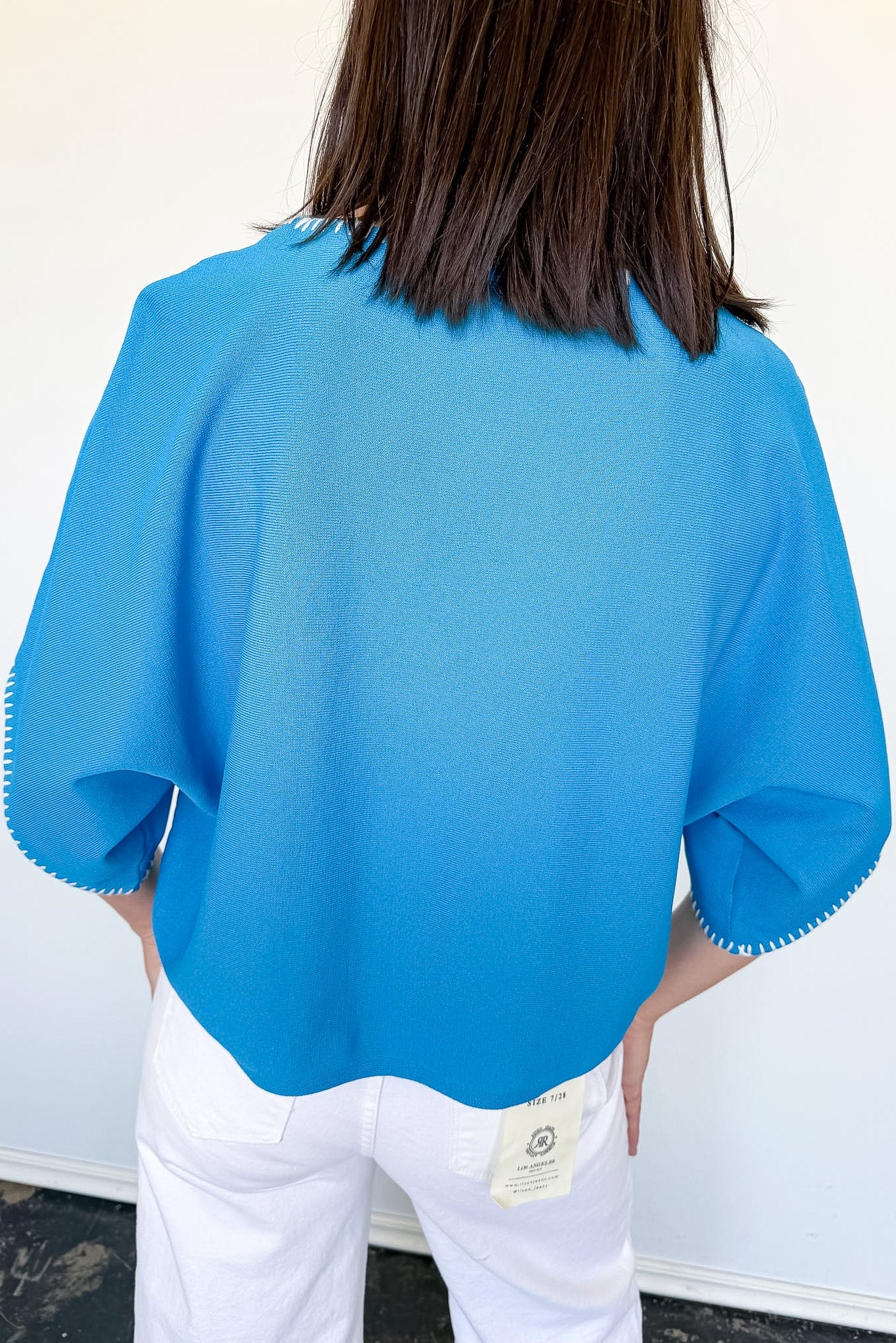 Person wearing a blue textured top with white pants against a plain background