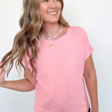 Woman wearing a pink top with a subtle pattern against a plain background