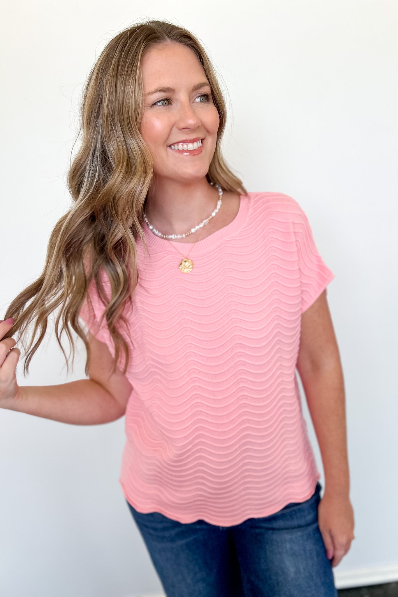 Woman wearing a pink top with a subtle pattern against a plain background