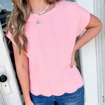 Woman wearing a pink scalloped hem top and blue jeans standing in front of a door.