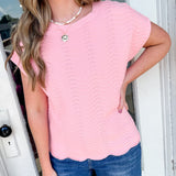 Woman wearing a pink scalloped hem top and blue jeans standing in front of a door.