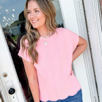 Woman wearing a pink top and blue jeans standing in front of a door.
