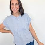 Woman wearing a light blue striped shirt and jeans against a white wall