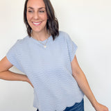Woman wearing a light blue striped shirt and jeans against a white wall