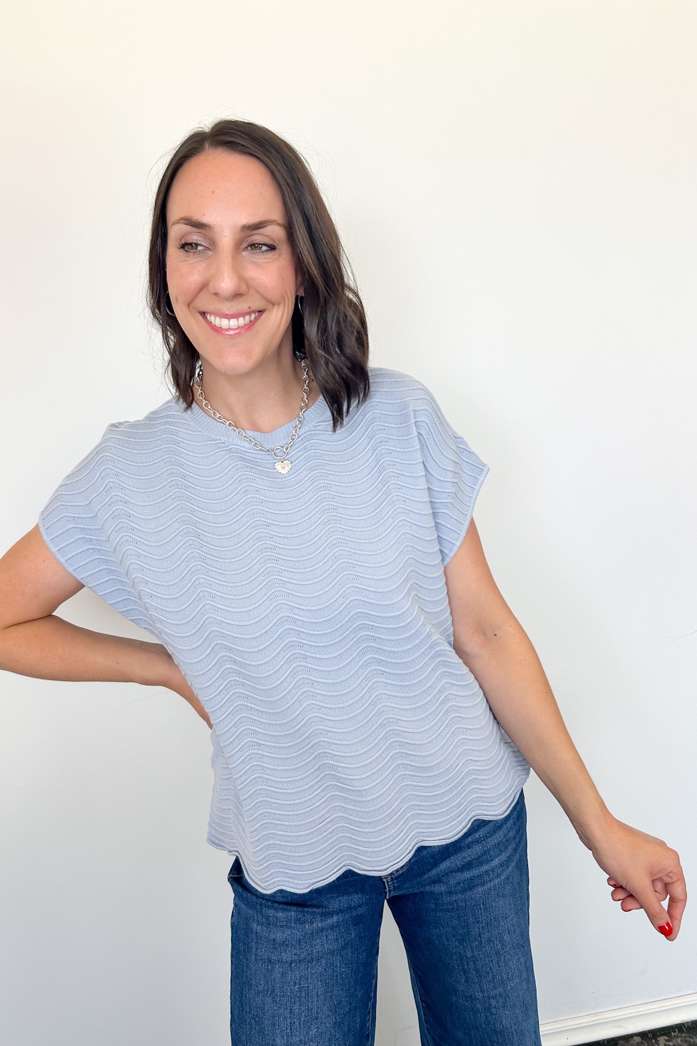 Woman wearing a light blue striped shirt and jeans against a white wall