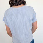 Person wearing a light blue striped shirt and blue jeans against a white wall.