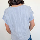 Person wearing a light blue striped shirt and blue jeans against a white wall.