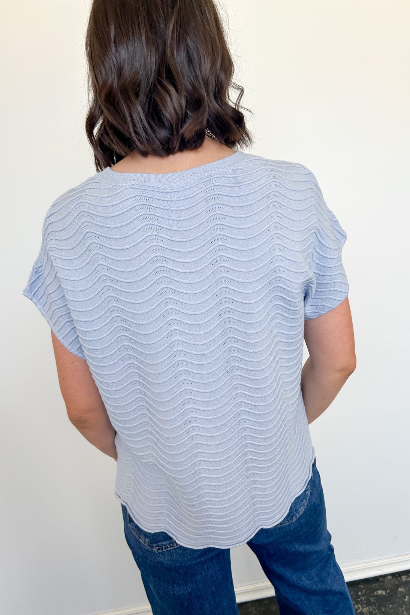 Person wearing a light blue striped shirt and blue jeans against a white wall.