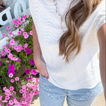 Person wearing a white top and light blue jeans standing next to pink flowers.