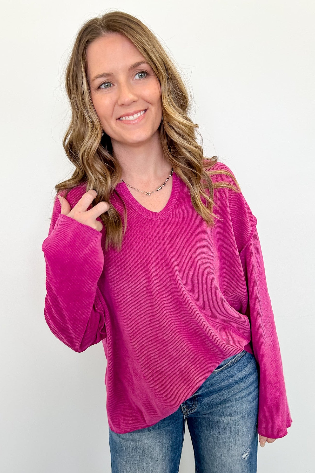 Woman wearing a bright pink sweater and blue jeans against a white background