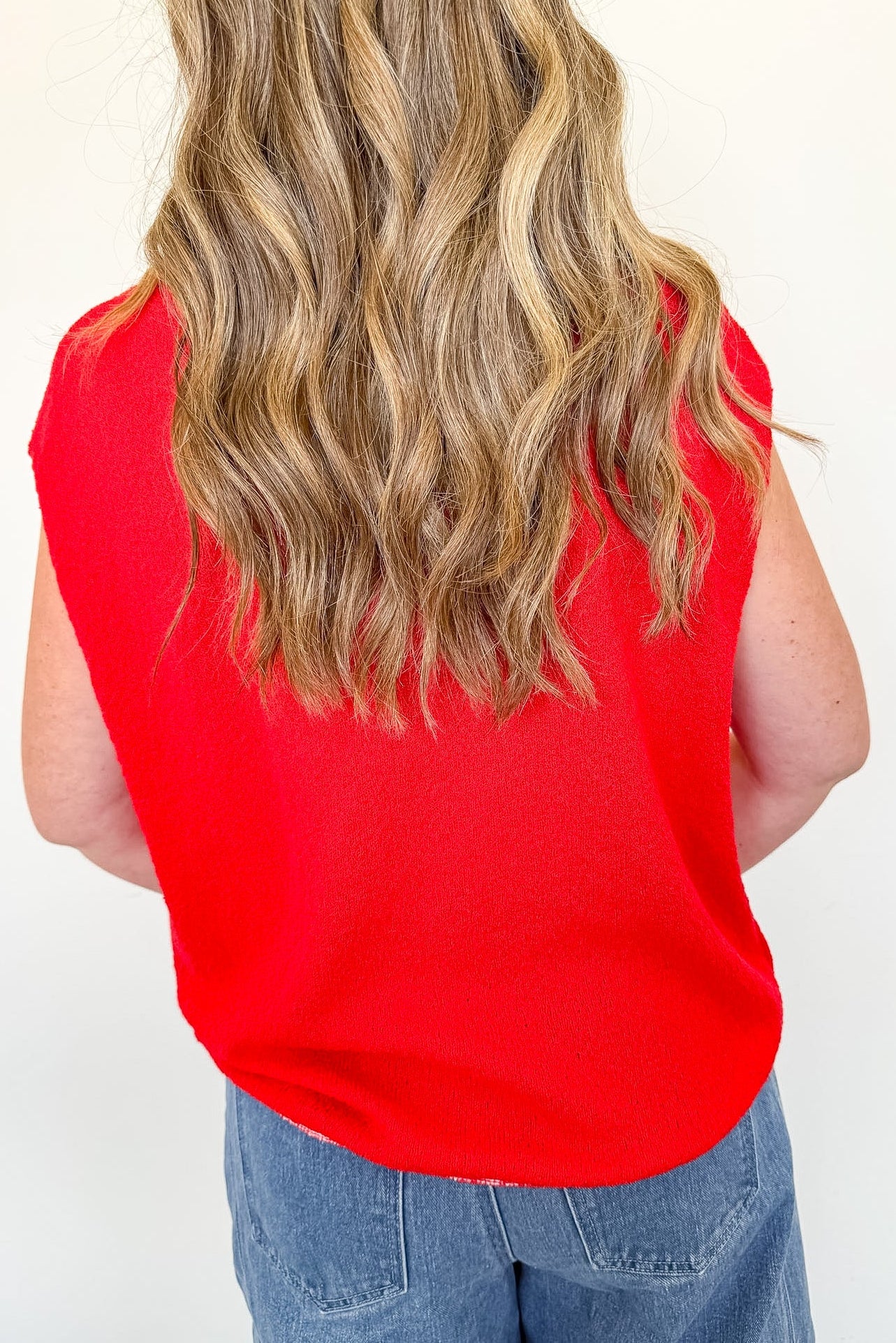 Person wearing a red sleeveless top and blue jeans against a white background
