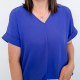 Woman wearing a blue v neckline top with white shorts and her hand in her pocket.
