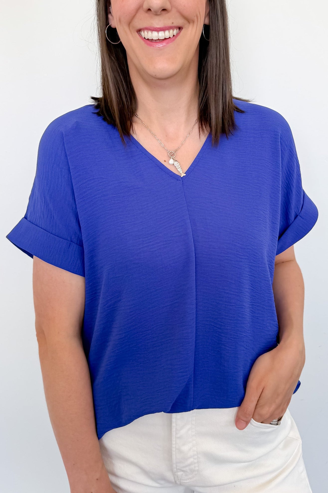 Woman wearing a blue v neckline top with white shorts and her hand in her pocket.