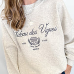 Person wearing a beige sweatshirt with 'Chateau des Vignes' text and design.