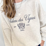 Person wearing a beige sweatshirt with 'Chateau des Vignes' text and design.