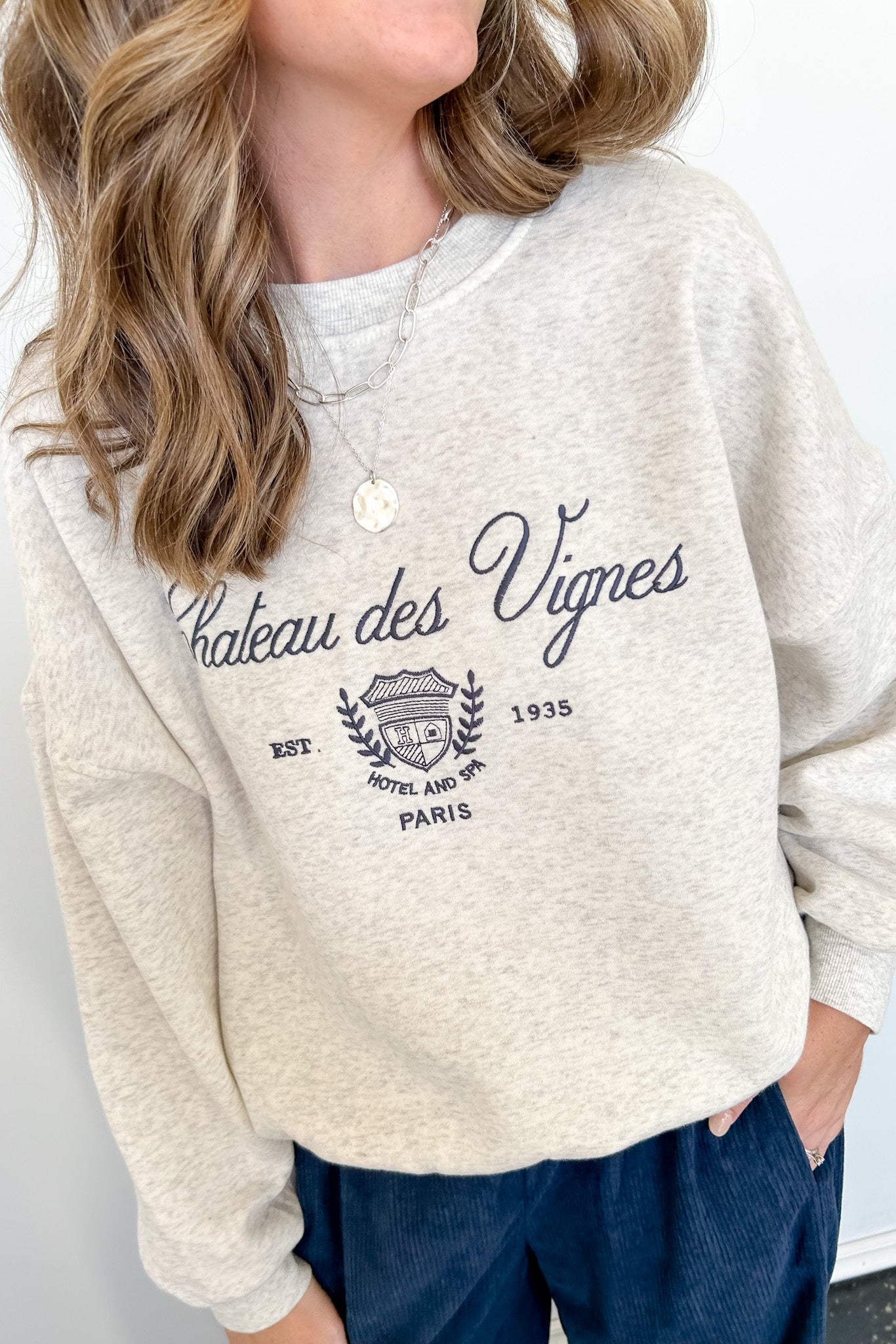 Person wearing a beige sweatshirt with 'Chateau des Vignes' text and design.