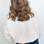 Person wearing a white textured sweater and blue pants against a white wall