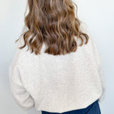 Person wearing a white textured sweater and blue pants against a white wall