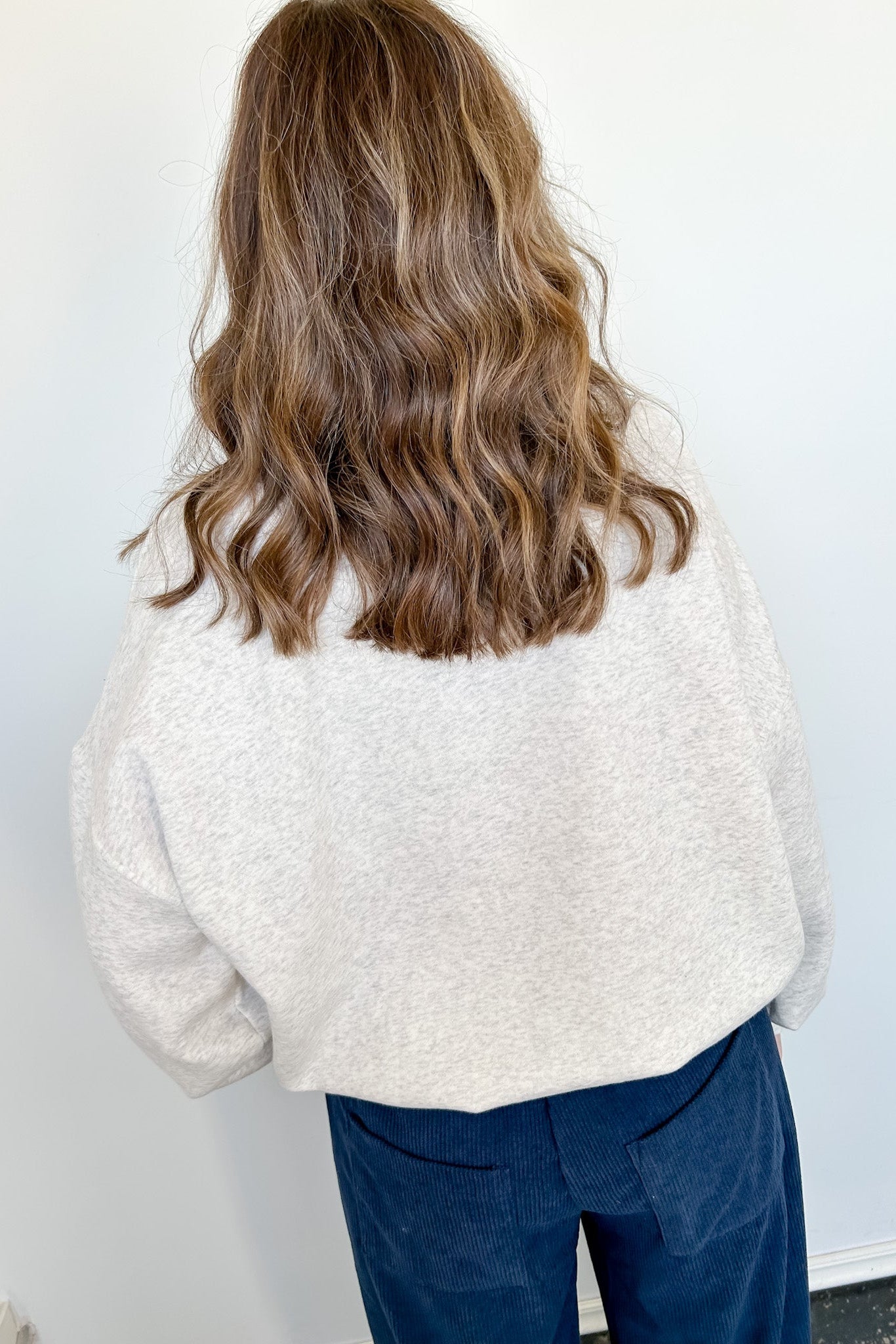 Person wearing a white textured sweater and blue pants against a white wall