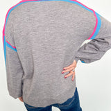Person wearing a gray sweater with pink and blue accents against a white background