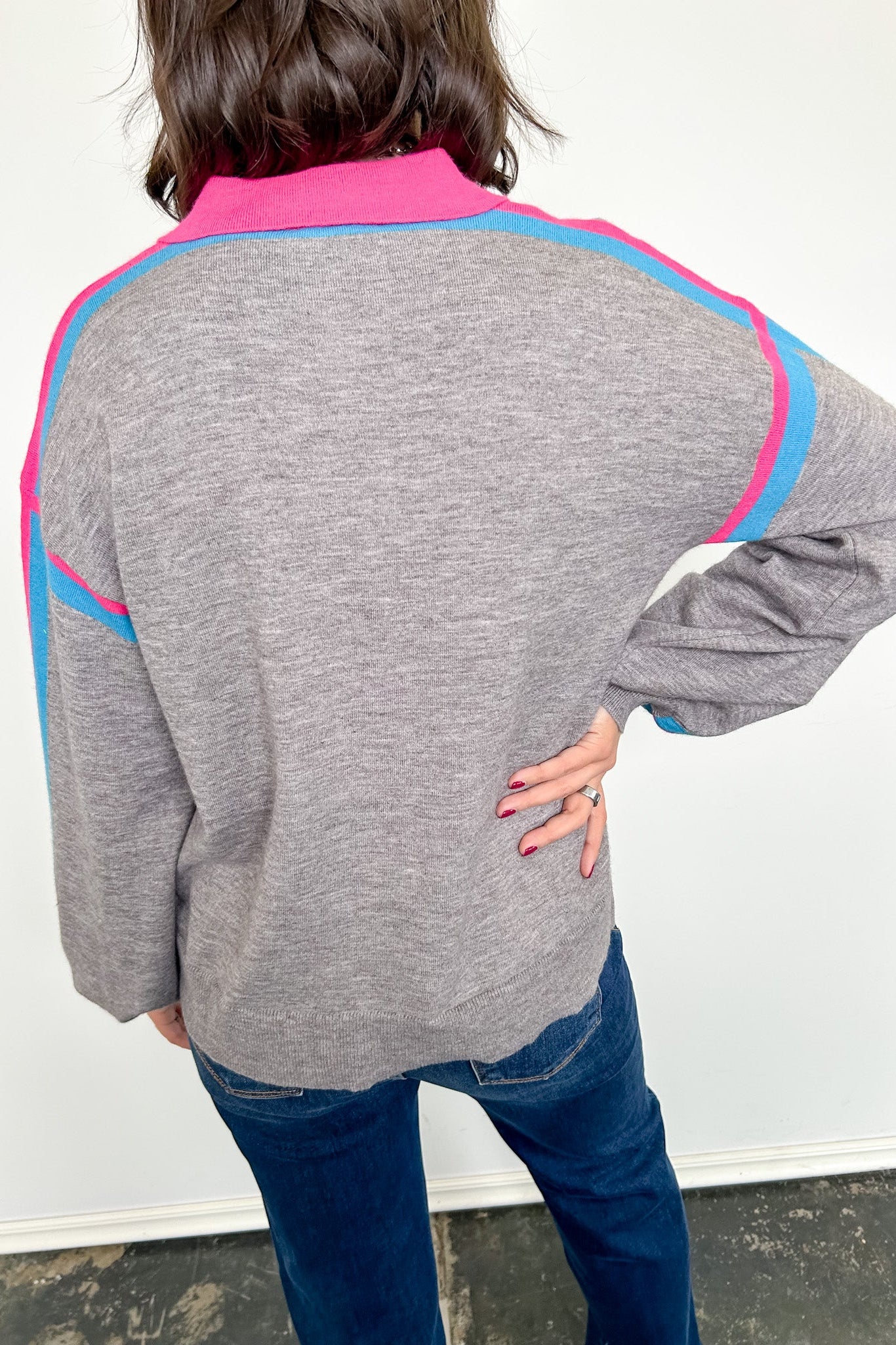 Person wearing a gray sweater with pink and blue accents against a white background