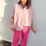 Woman wearing a pink shirt and pants against a white wall.