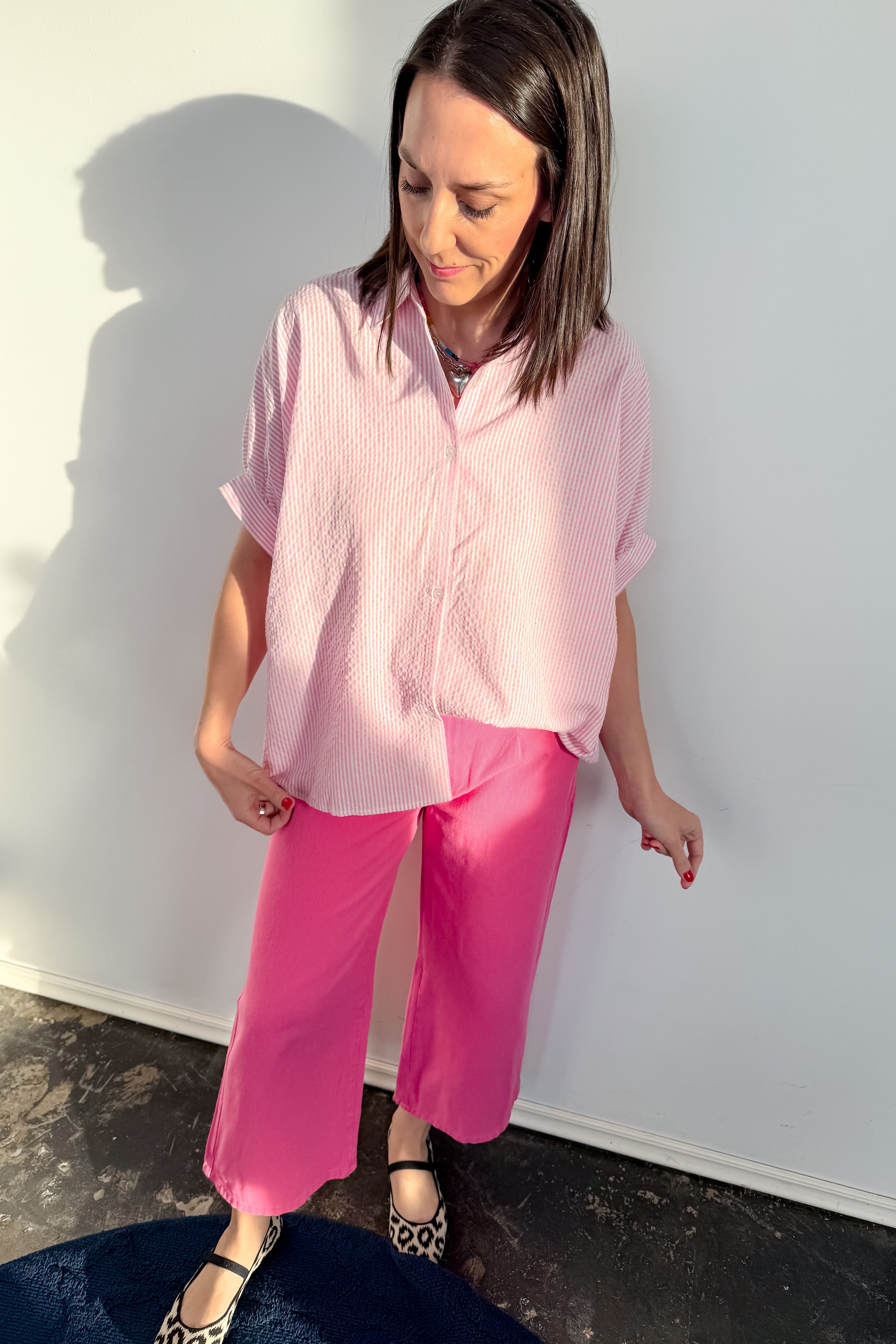 Woman wearing a pink shirt and pants against a white wall.