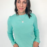 Woman wearing a teal long-sleeve top against a white background