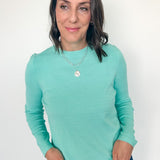 Woman wearing a teal long-sleeve top against a white background