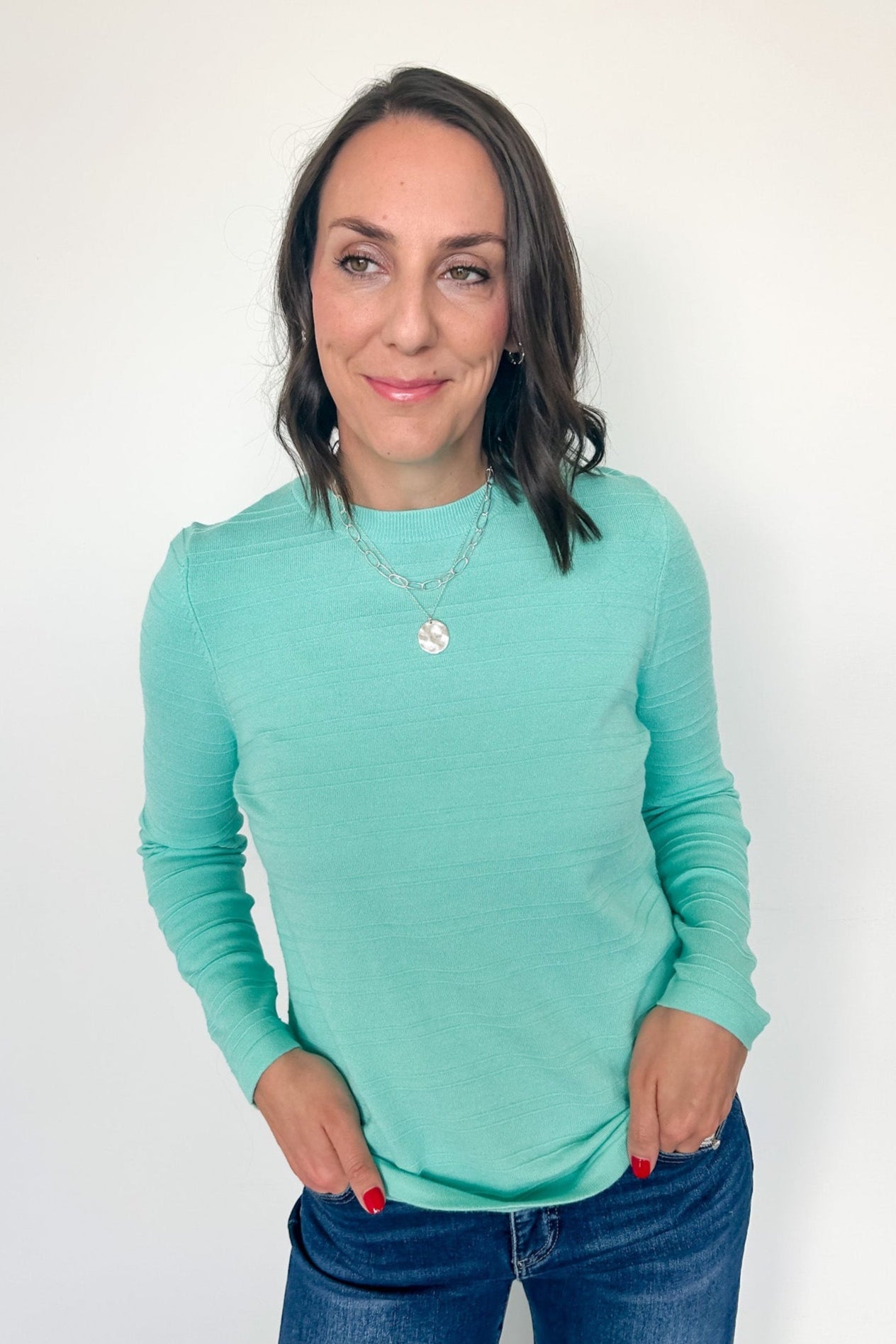 Woman wearing a teal long-sleeve top against a white background
