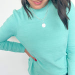 Woman wearing a light blue long-sleeve top and jeans against a white background