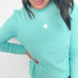 Woman wearing a light blue long-sleeve top and jeans against a white background