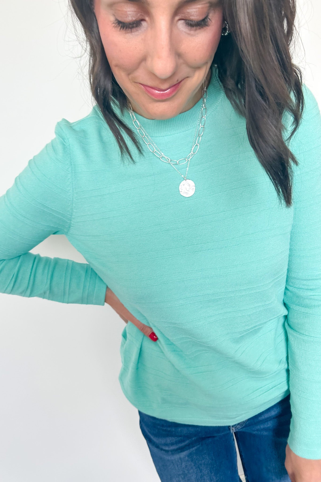 Woman wearing a light blue long-sleeve top and jeans against a white background