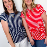 Two women wearing striped shirts standing against a white wall.