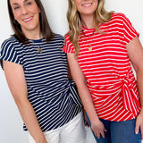 Two women wearing striped shirts standing against a white wall.
