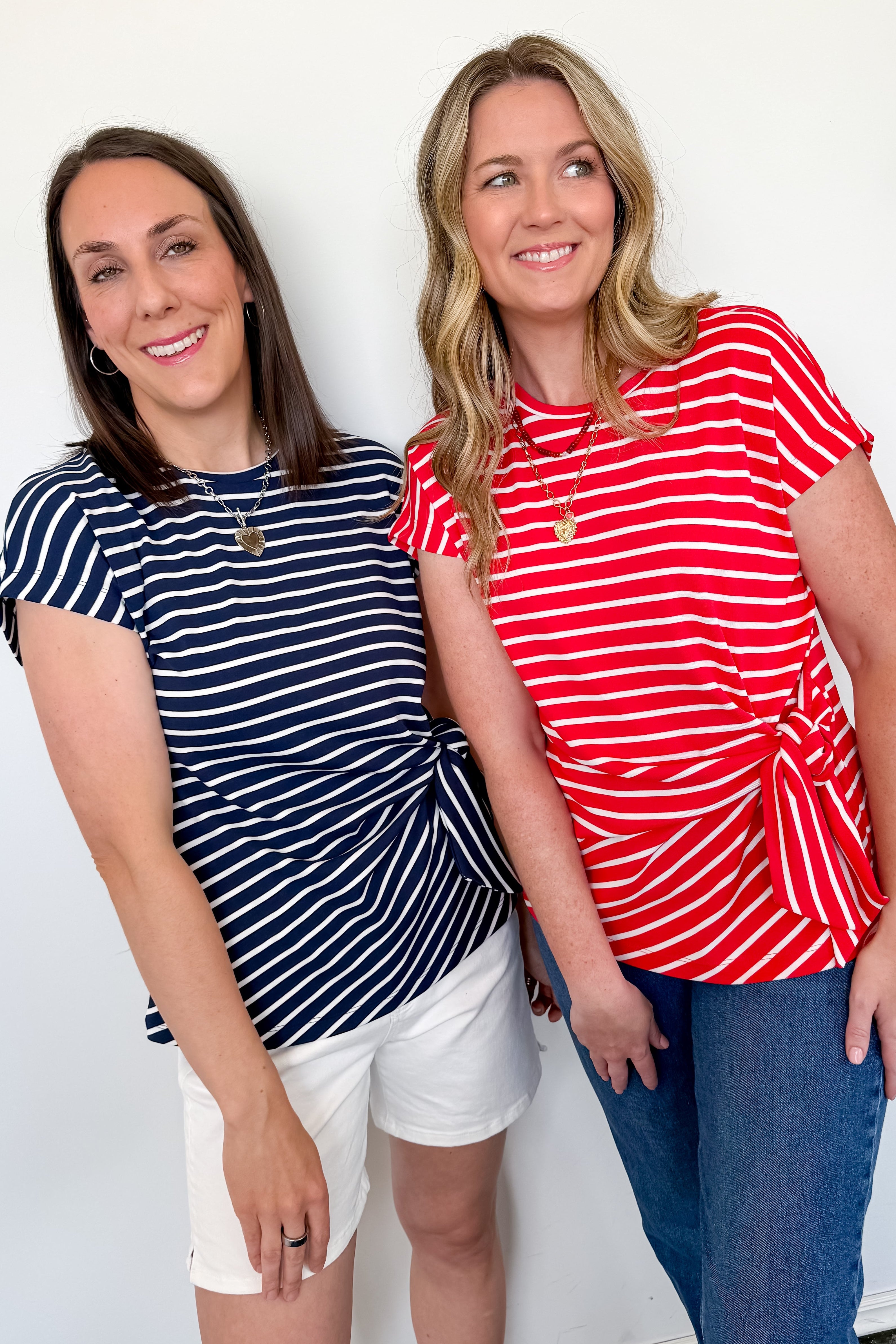 Two women wearing striped shirts standing against a white wall.