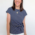 Woman wearing a navy and white striped shirt with white shorts against a plain background