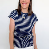 Woman wearing a navy and white striped shirt with white shorts against a plain background