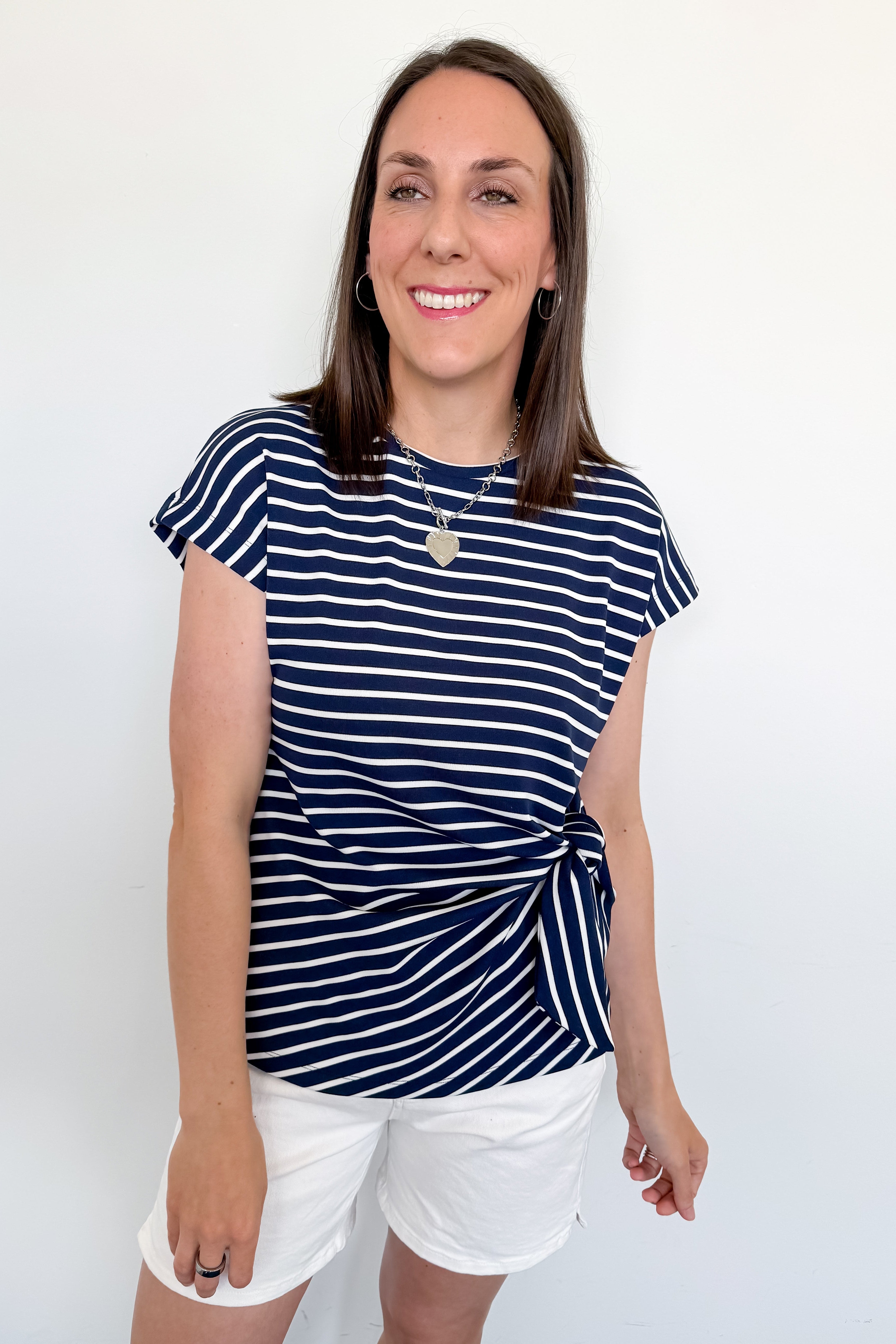 Woman wearing a navy and white striped shirt with white shorts against a plain background