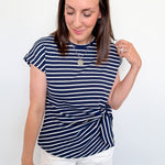 Woman wearing a navy striped shirt and white shorts against a plain background