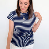 Woman wearing a navy striped shirt and white shorts against a plain background