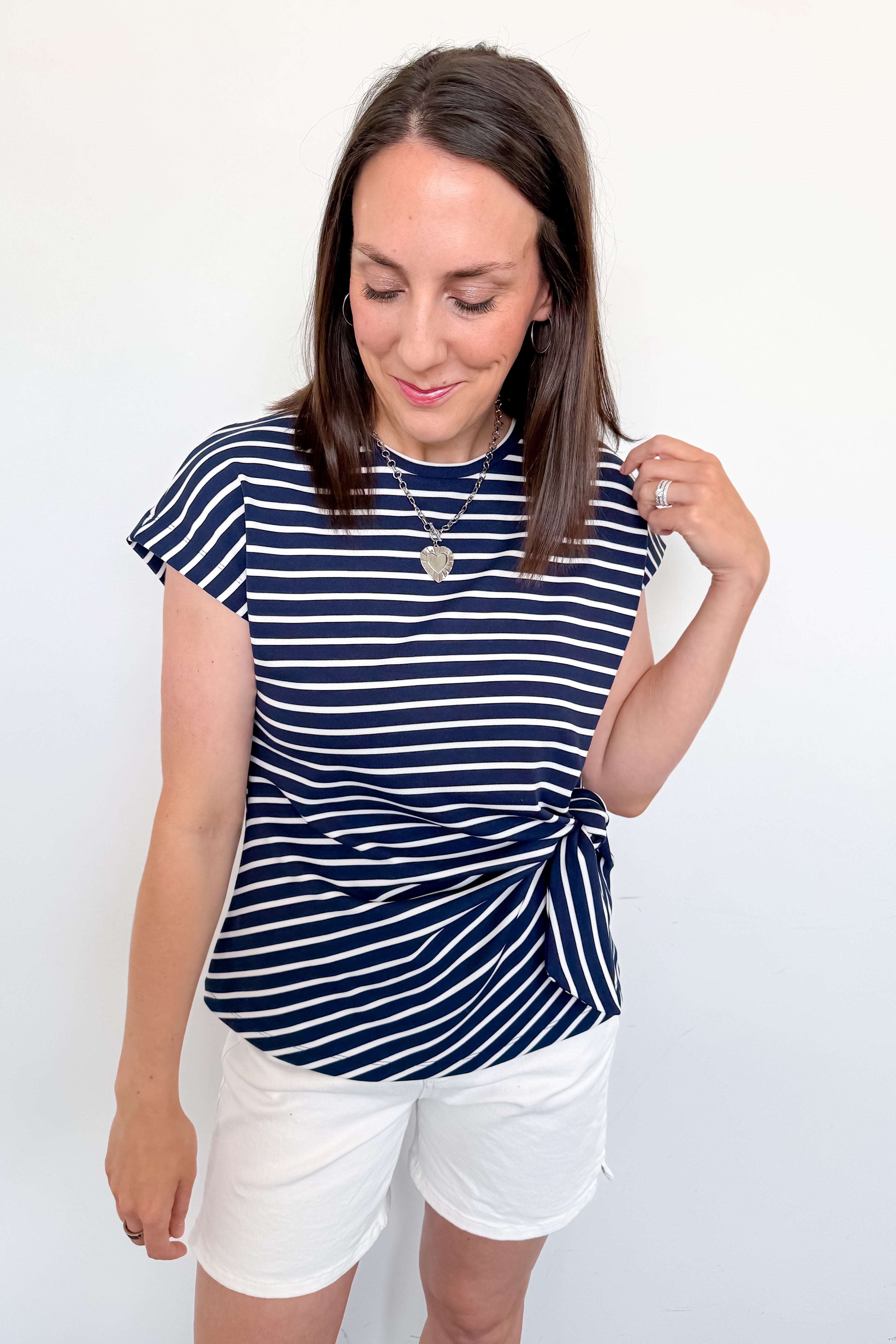 Woman wearing a navy striped shirt and white shorts against a plain background