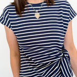 Woman wearing a navy and white striped t-shirt with a knot detail on a plain background