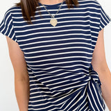 Woman wearing a navy and white striped t-shirt with a knot detail on a plain background