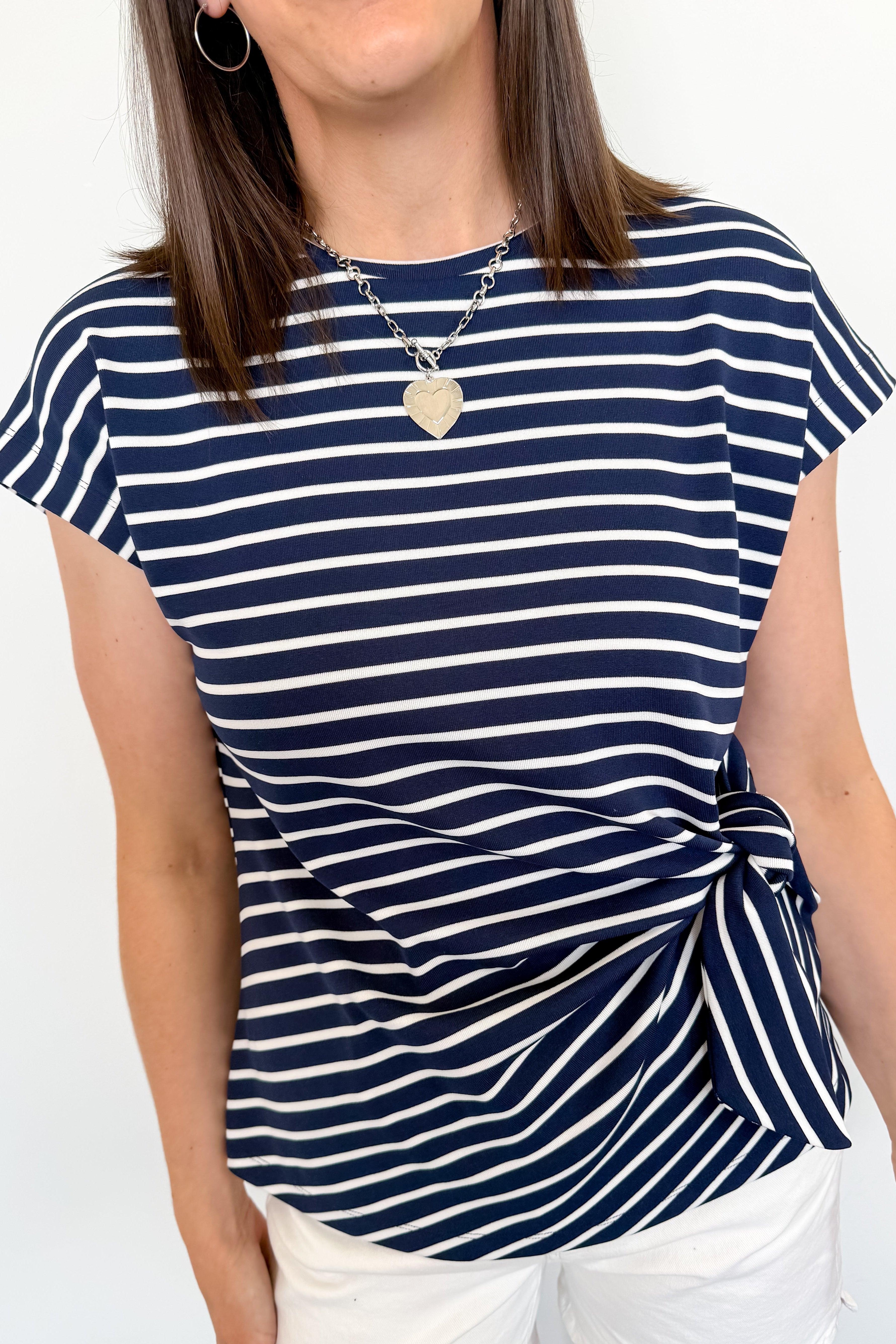 Woman wearing a navy and white striped t-shirt with a knot detail on a plain background