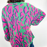 Person wearing a colorful leopard print cardigan against a white wall.