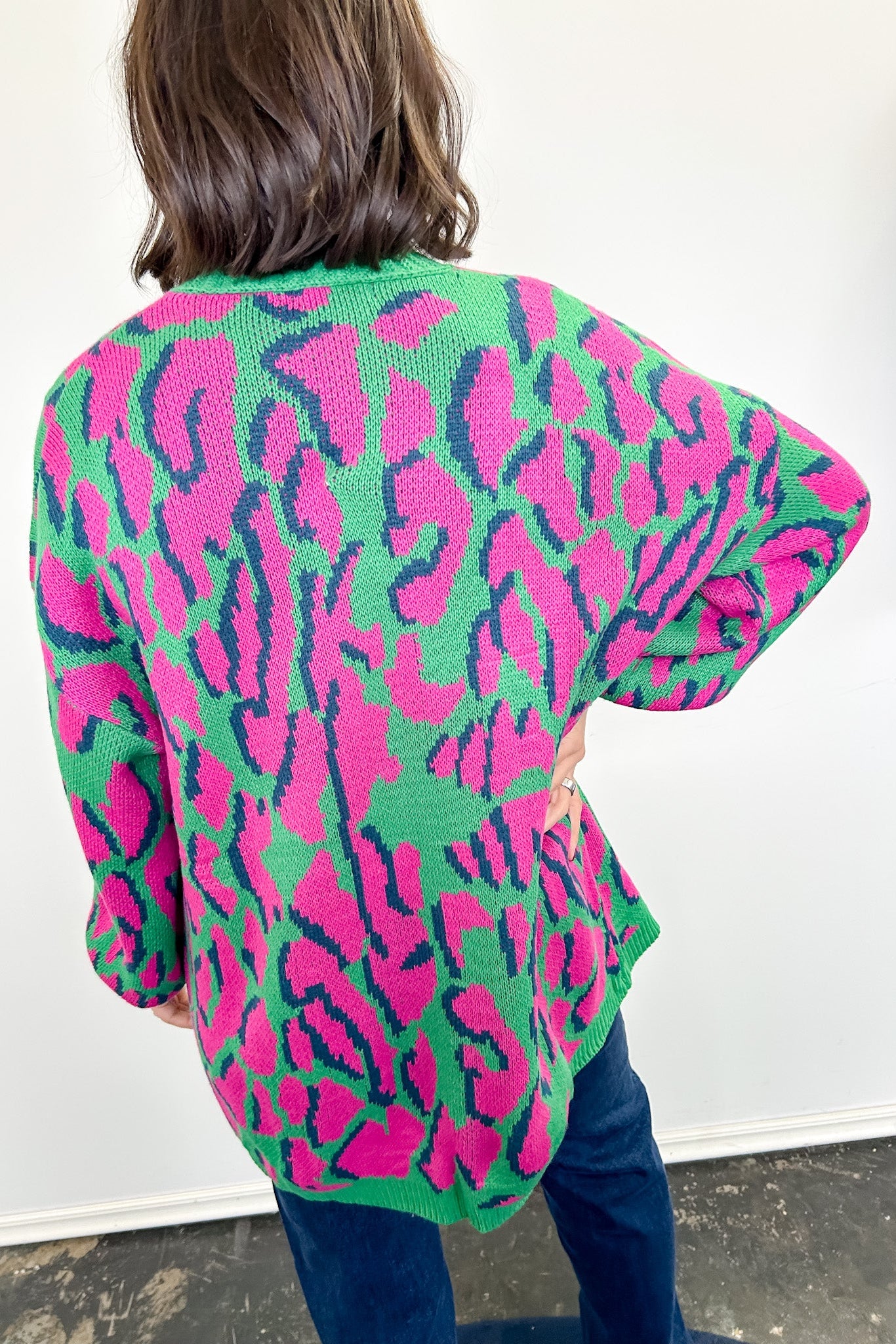 Person wearing a colorful leopard print cardigan against a white wall.